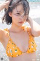 A woman in a yellow bikini standing on the beach.