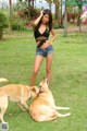 A woman in a black top and denim shorts playing with two dogs.