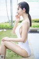 A woman in a white bathing suit sitting by a pool.