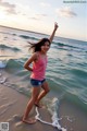 A young woman standing on the beach with her arms outstretched.