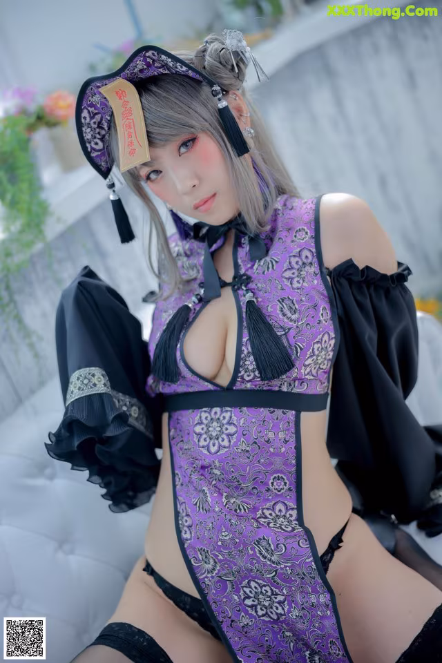 A woman in a purple and black lingerie sitting on a white couch.