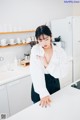 A woman in a white shirt and black skirt standing in a kitchen.