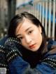 A woman in a blue and black sweater leaning against a fence.