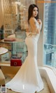A woman in a white dress standing by a window.