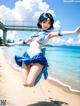 A woman in a blue and white outfit is jumping on the beach.